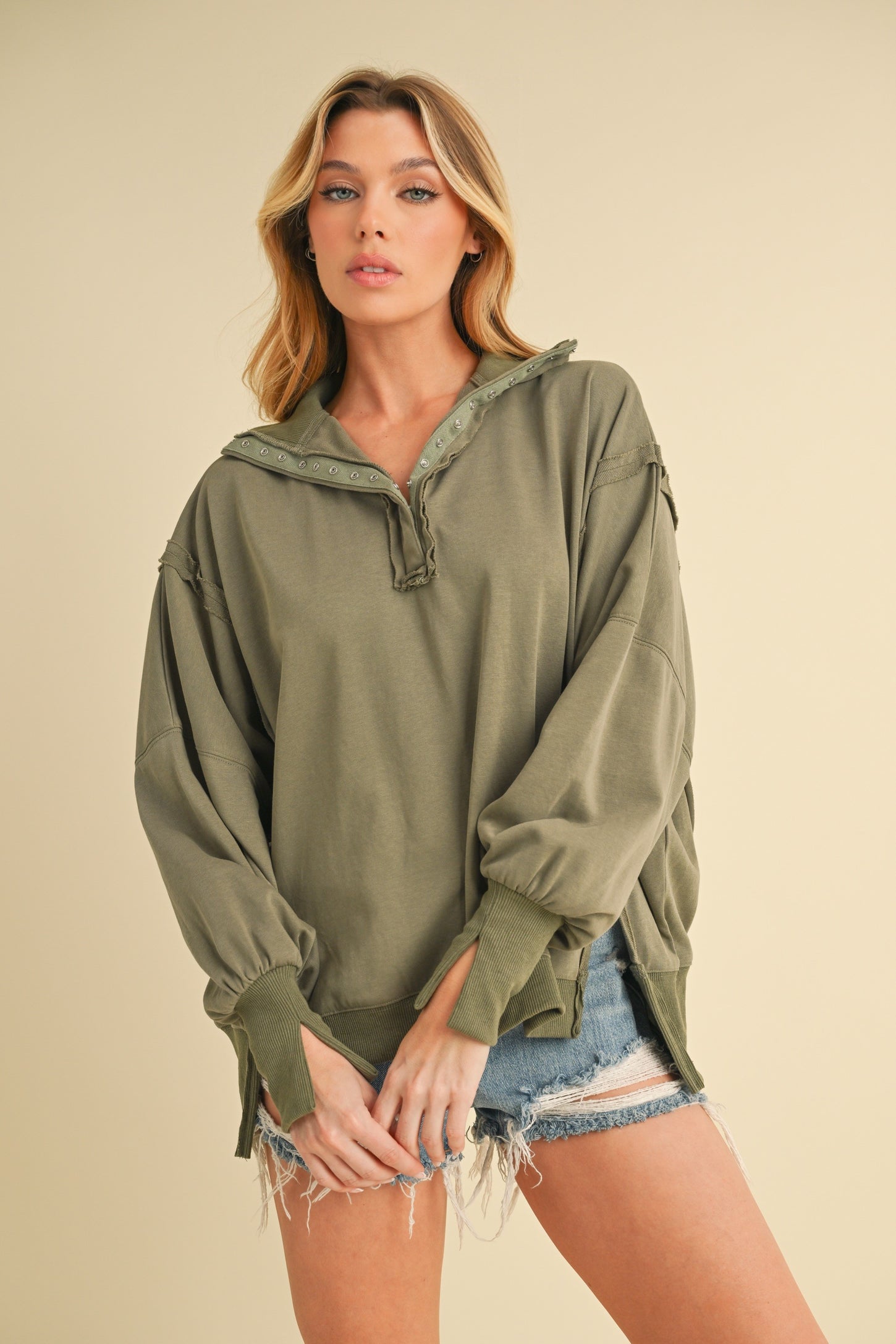 woman wearing an olive green oversized pullover sweatshirt with a half-zip and rolled sleeves, paired with denim shorts