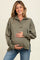 woman wearing an olive green maternity pullover with a half zip, holding her baby bump and smiling