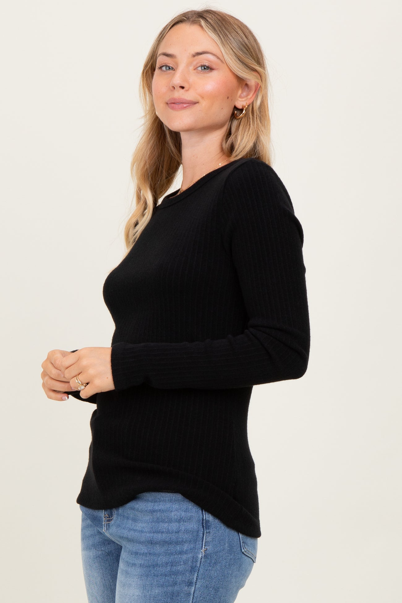 woman wearing a black ribbed long sleeve sweater with a curved hem and standing sideways