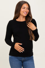 woman wearing a black ribbed maternity top and holding her baby bump
