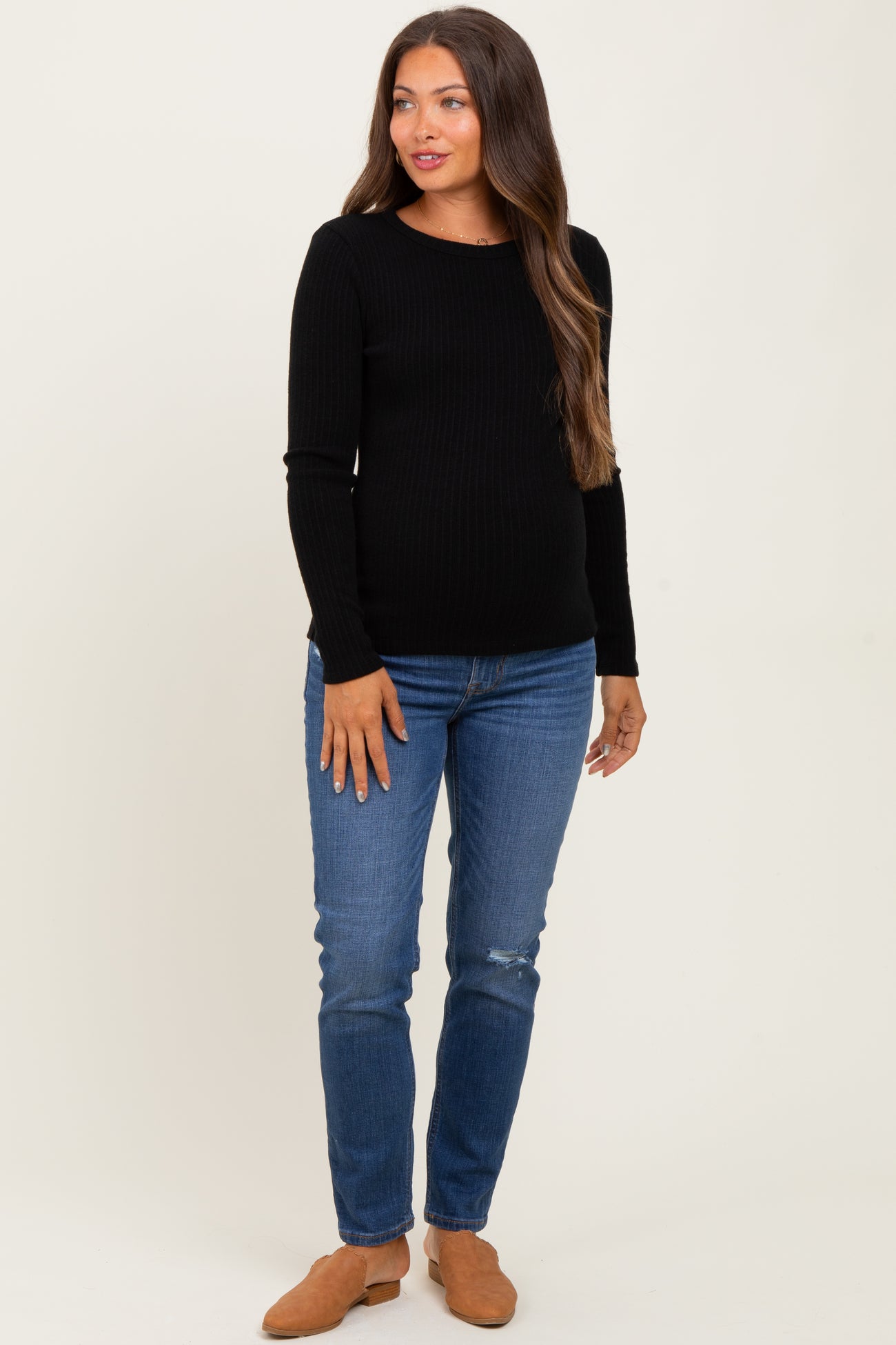 woman wearing a black ribbed long sleeve maternity top and blue distressed skinny jeans with a baby bump visible