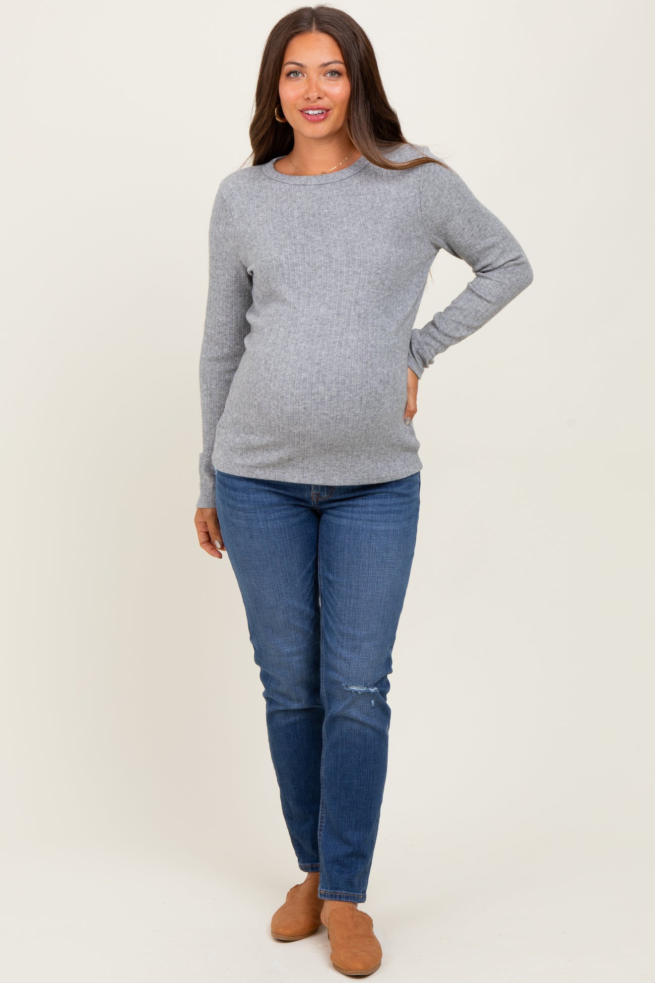 woman wearing a light gray long sleeve maternity top and blue skinny jeans showing her baby bump