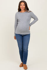 woman wearing a light gray long sleeve maternity top and blue skinny jeans showing her baby bump