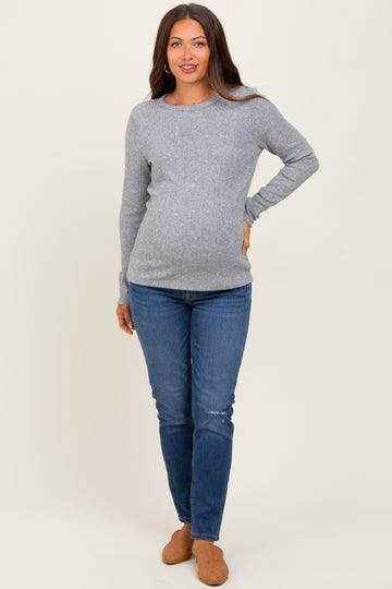 woman wearing a light gray long sleeve maternity top and blue skinny jeans showing her baby bump