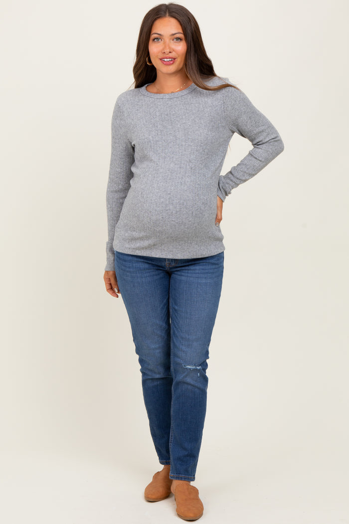 woman wearing a light gray long sleeve maternity top and blue skinny jeans showing her baby bump