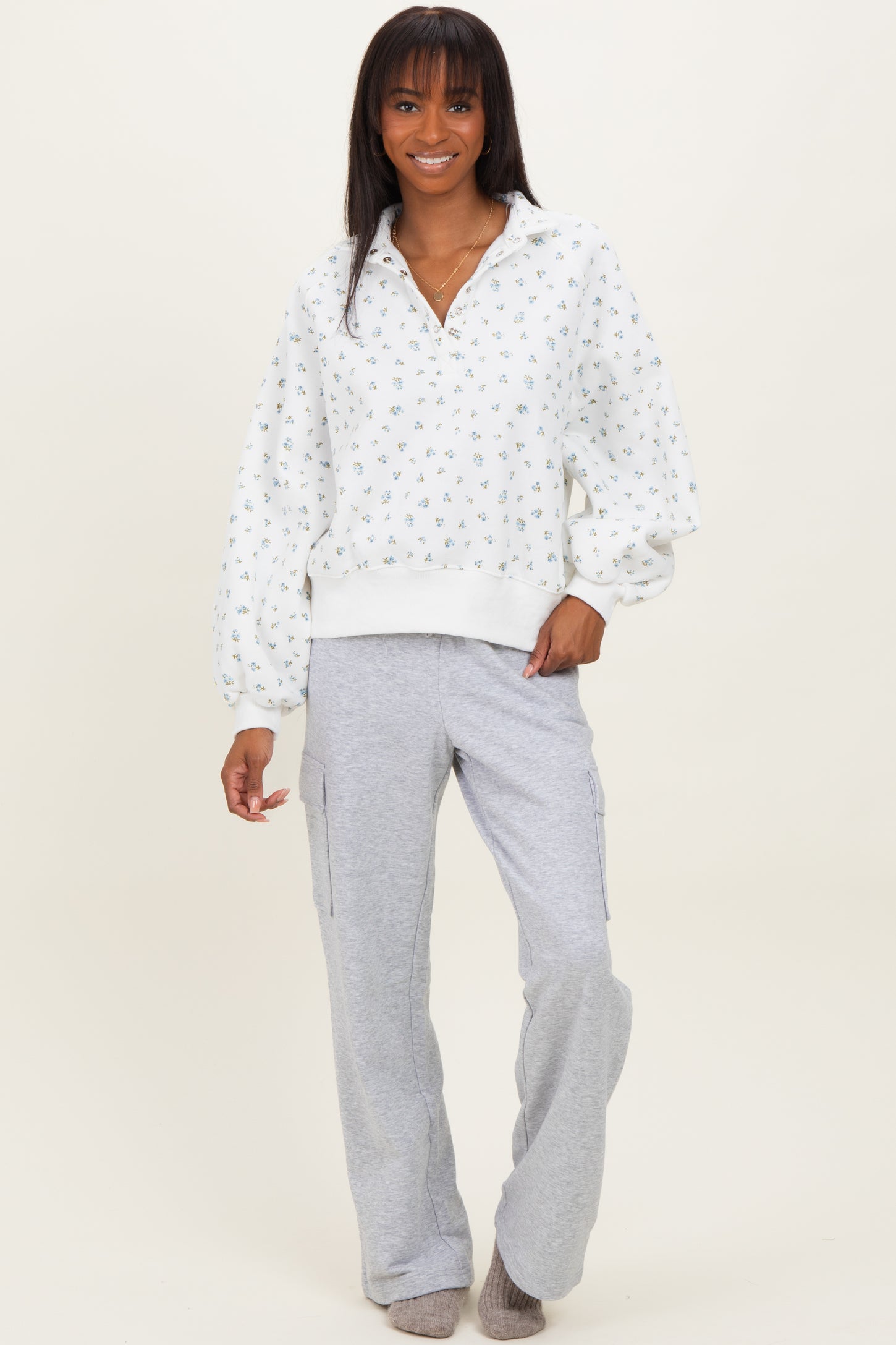 woman wearing a white floral patterned pullover sweatshirt with balloon sleeves and gray cargo sweatpants