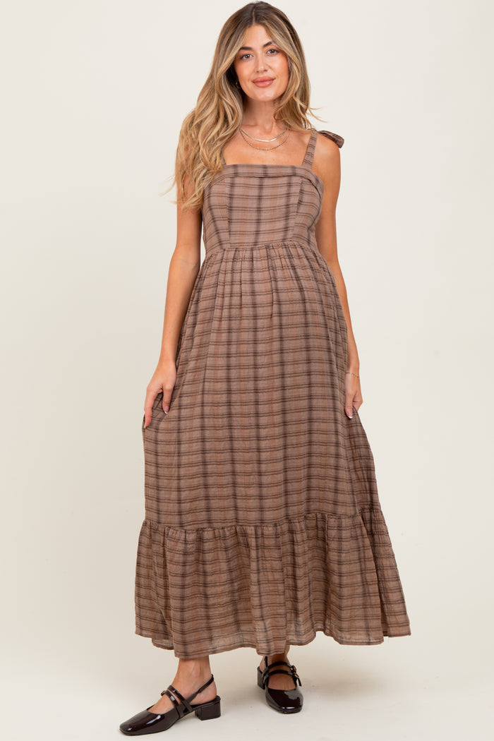 woman wearing a brown striped maxi maternity dress with a square neckline and tie straps, showing a visible baby bump