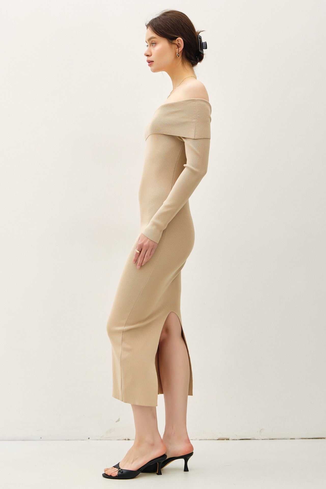 woman wearing a beige off-shoulder ribbed midi dress with a side slit and black high heel sandals