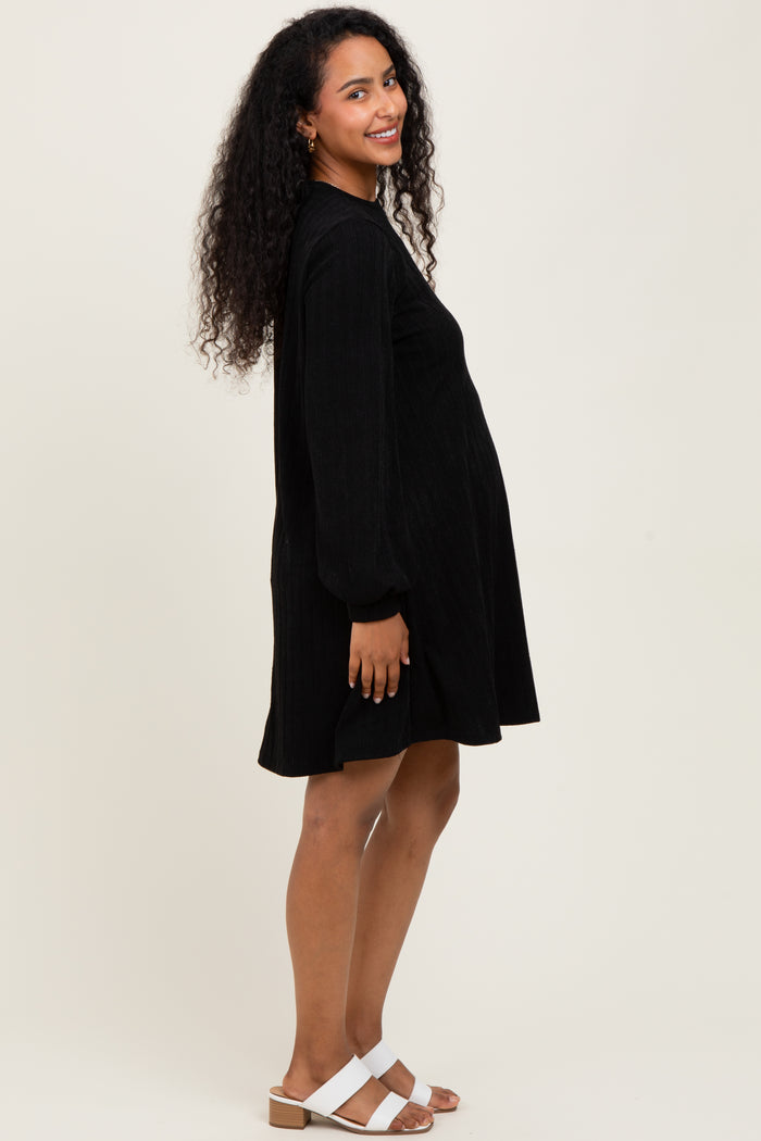 woman wearing a black corduroy maternity dress with puff sleeves and a visible baby bump