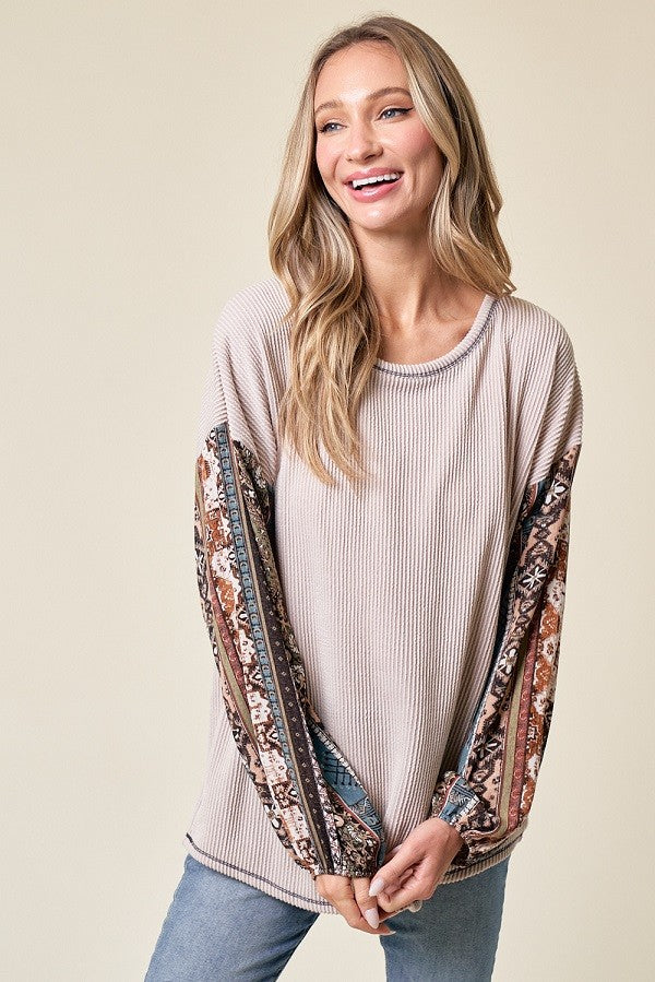 woman wearing a beige ribbed long sleeve top with patterned sleeves and smiling