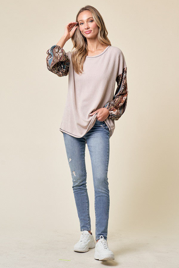 woman wearing a beige oversized top with patterned sleeves and light blue distressed skinny jeans