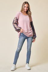woman wearing a pink ribbed long sleeve top with patterned sleeves and blue distressed jeans, standing on a beige background