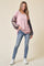 woman wearing a pink ribbed long sleeve top with patterned sleeves and blue distressed jeans, standing on a beige background