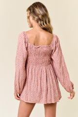 woman wearing a pink floral smocked mini dress with long sleeves and a square neckline, view from the back