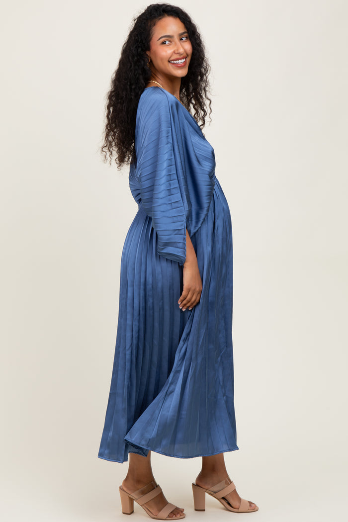 woman wearing a blue pleated maxi maternity dress, showcasing her baby bump and smiling at the camera