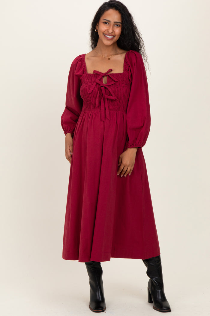 woman wearing a burgundy maternity dress with puff sleeves and a smocked bodice, styled with black knee-high boots