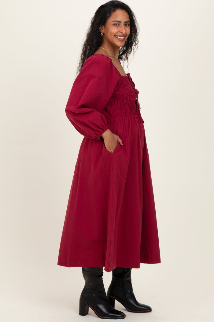 woman wearing a burgundy maternity dress with puff sleeves and pockets, showcasing her baby bump