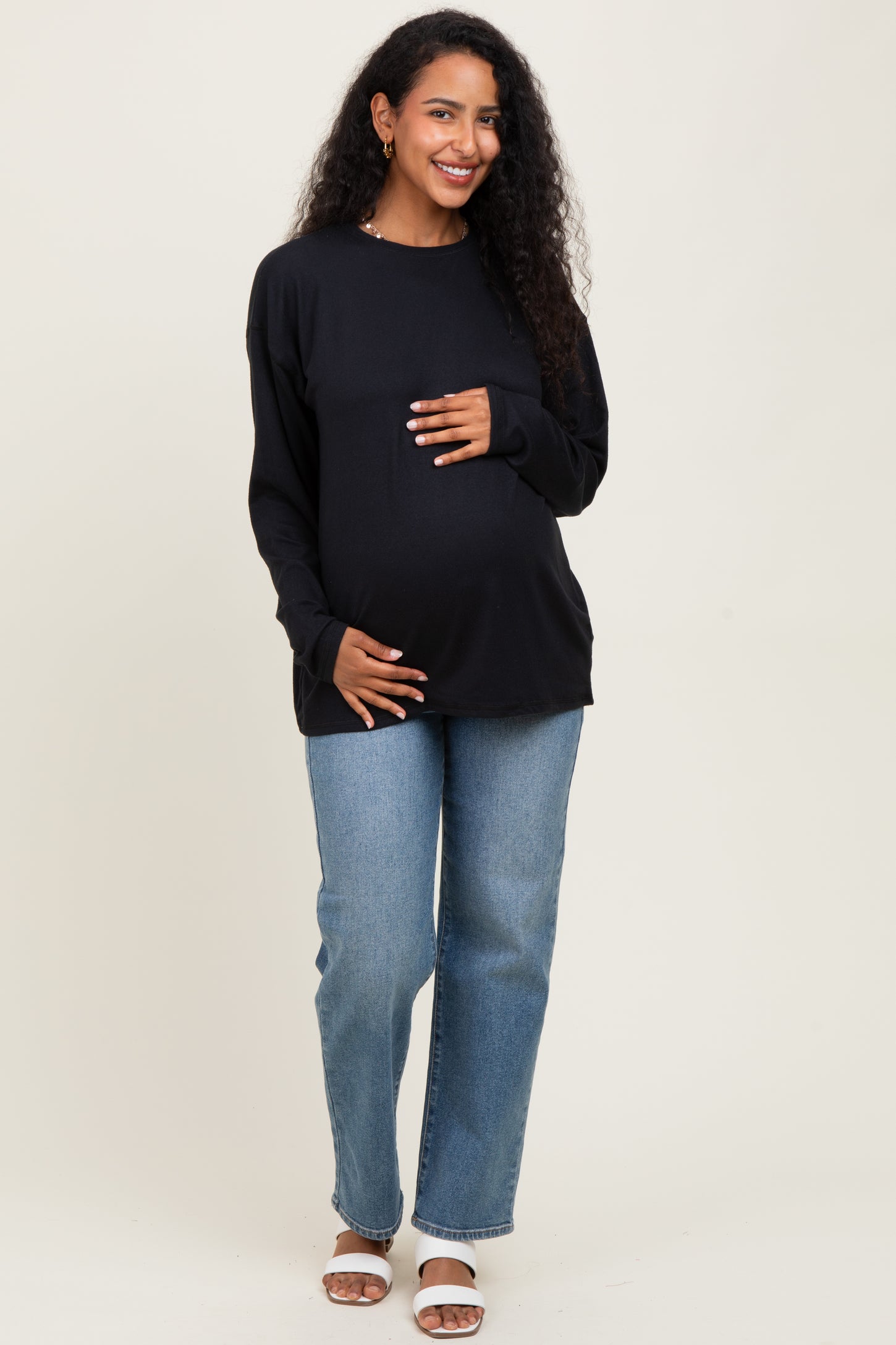 woman wearing a black long sleeve maternity top and holding her baby bump with light blue jeans