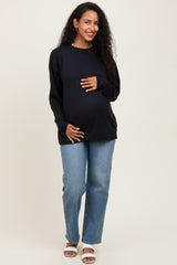 woman wearing a black long sleeve maternity top and holding her baby bump with light blue jeans