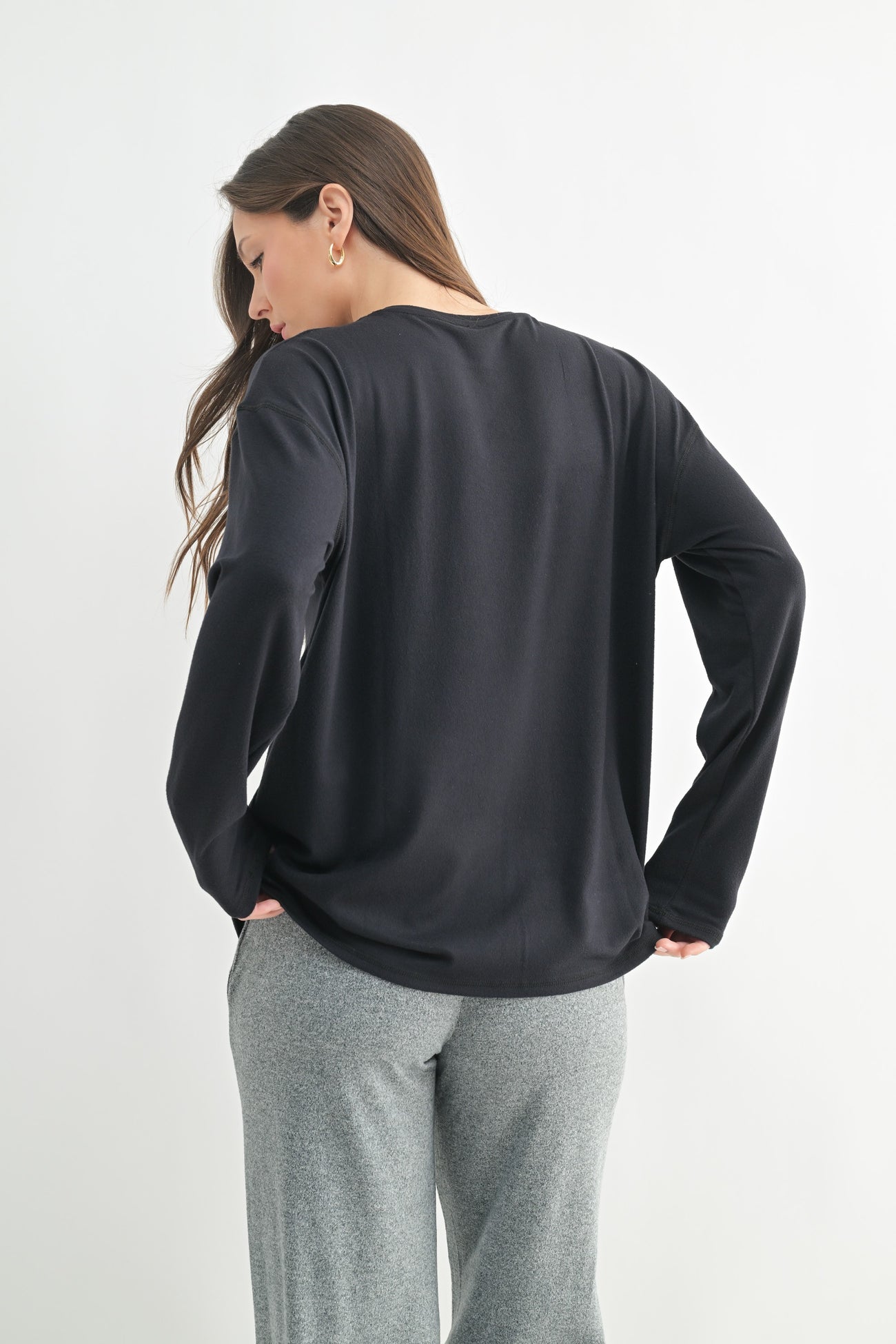 woman wearing a black long sleeve top with a relaxed fit, styled with gray sweatpants, viewed from the back
