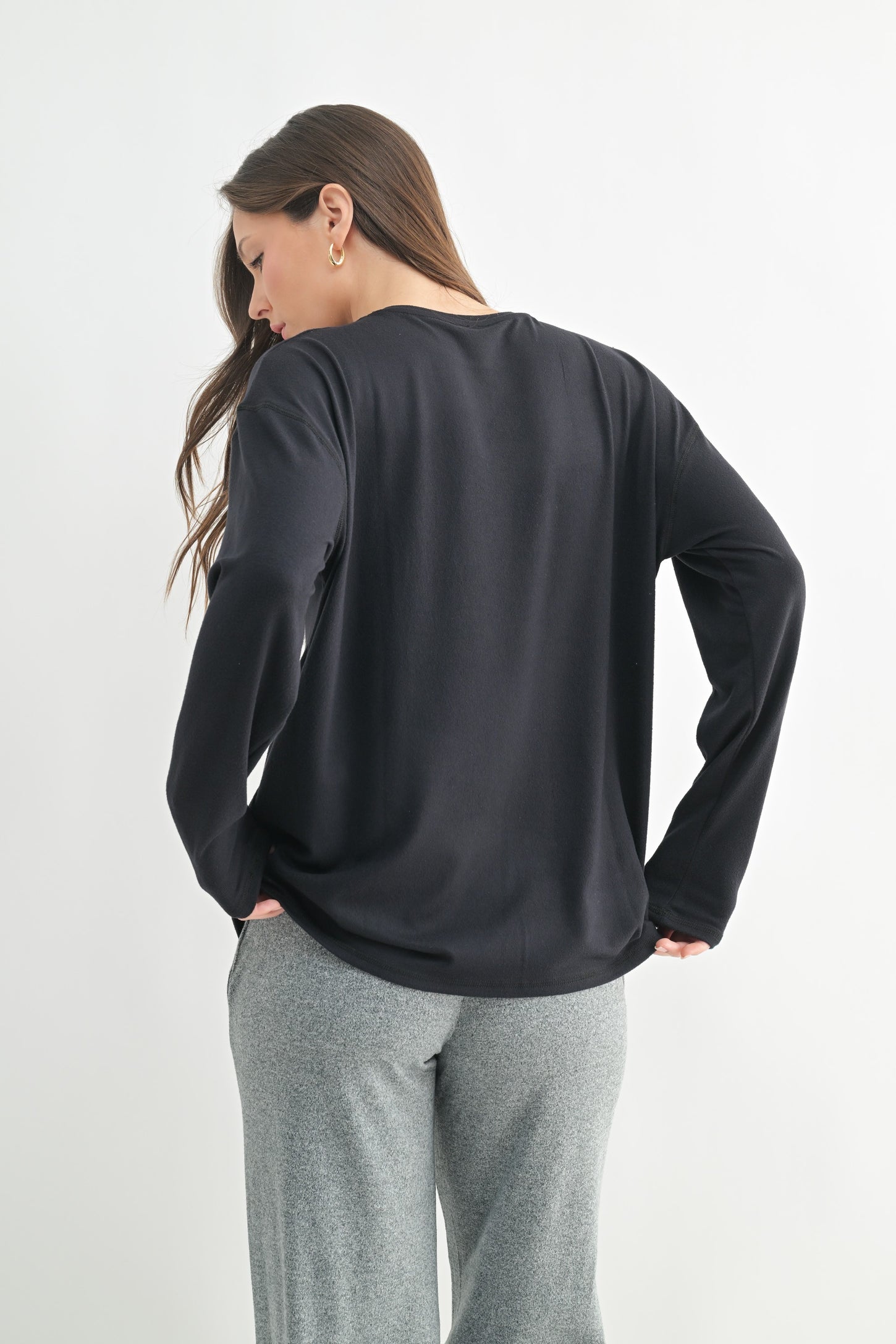 woman wearing a black long sleeve top with a relaxed fit, styled with gray sweatpants, viewed from the back