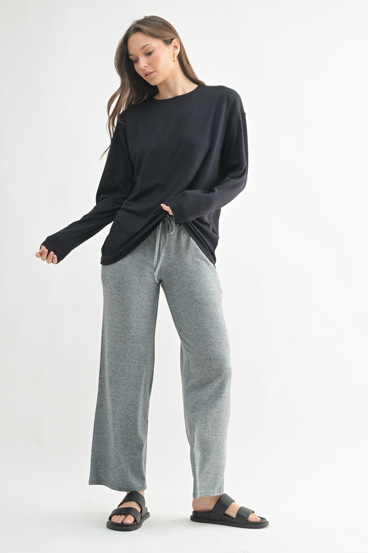 woman wearing a black long sleeve shirt and gray wide-leg lounge pants, standing in a relaxed pose