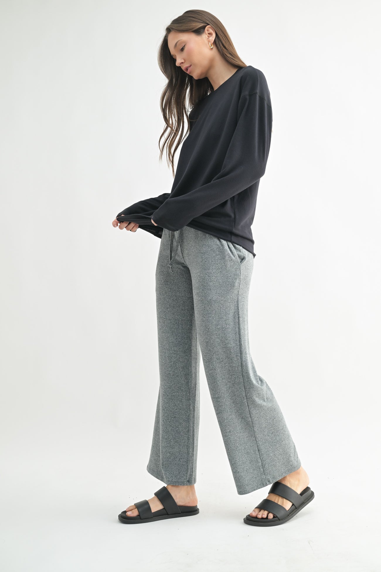 woman wearing a black long sleeve top with gray wide-leg pants and black slide sandals
