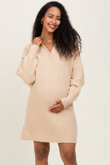 woman wearing a beige oversized v-neck maternity sweater dress and holding her baby bump