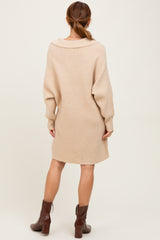 woman wearing a beige oversized sweater dress with a shawl collar and long sleeves, standing with her back to the camera