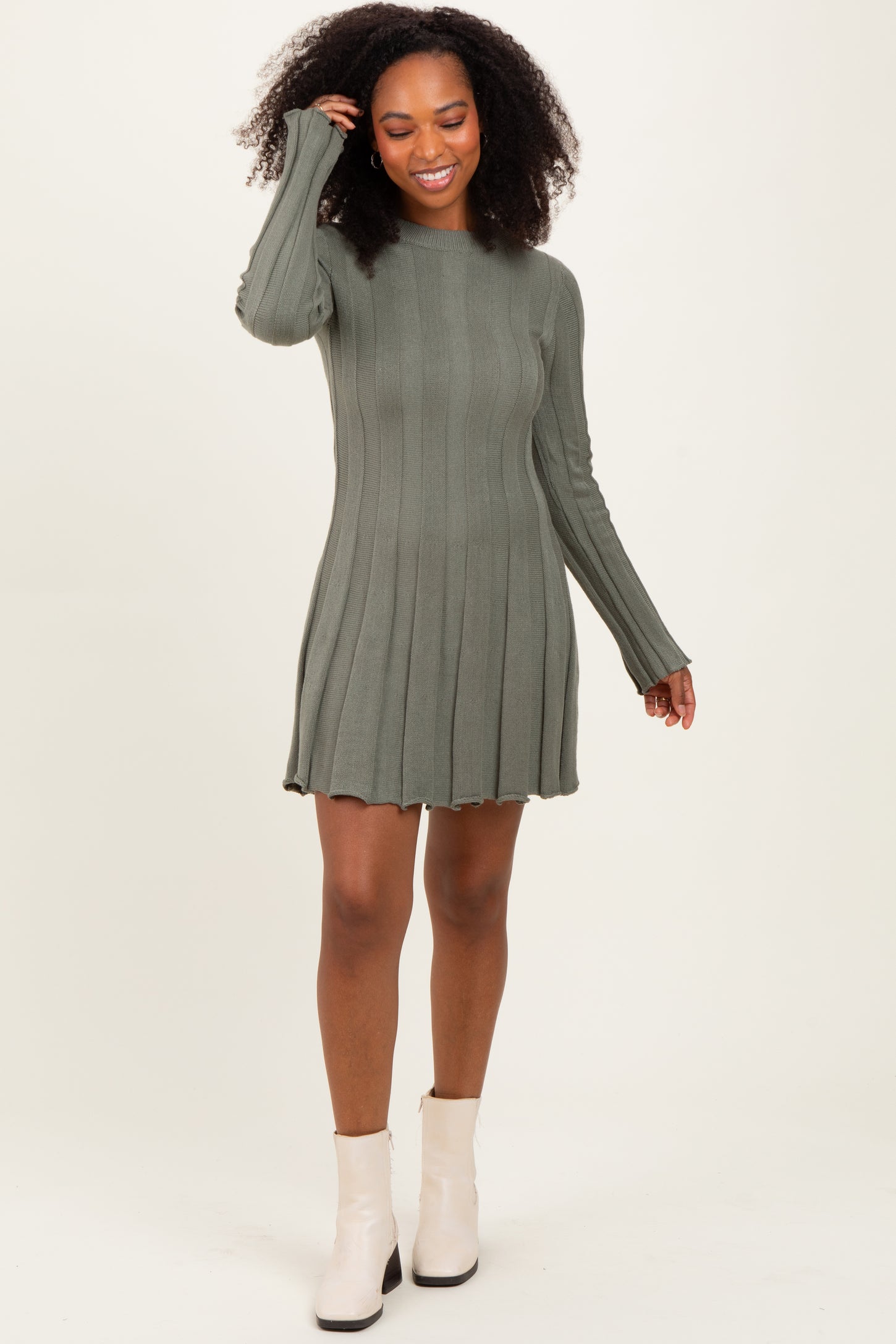 woman wearing a green ribbed long sleeve mini dress with a flared hem and smiling while posing