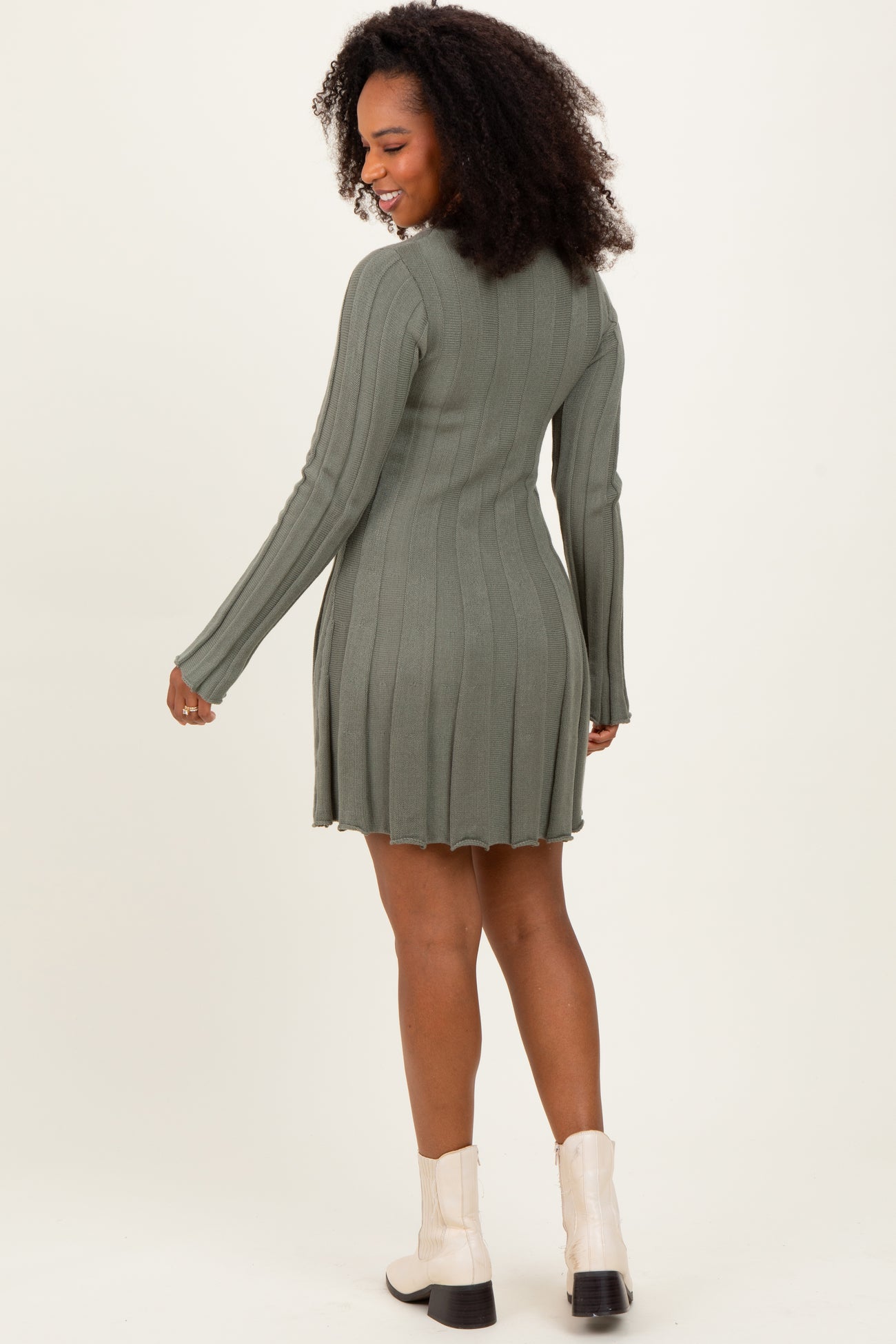 woman wearing a green ribbed long sleeve dress with a flared hem and styled with white ankle boots