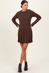 woman wearing a brown ribbed sweater dress with long sleeves and a flared hem, standing with hands on hips