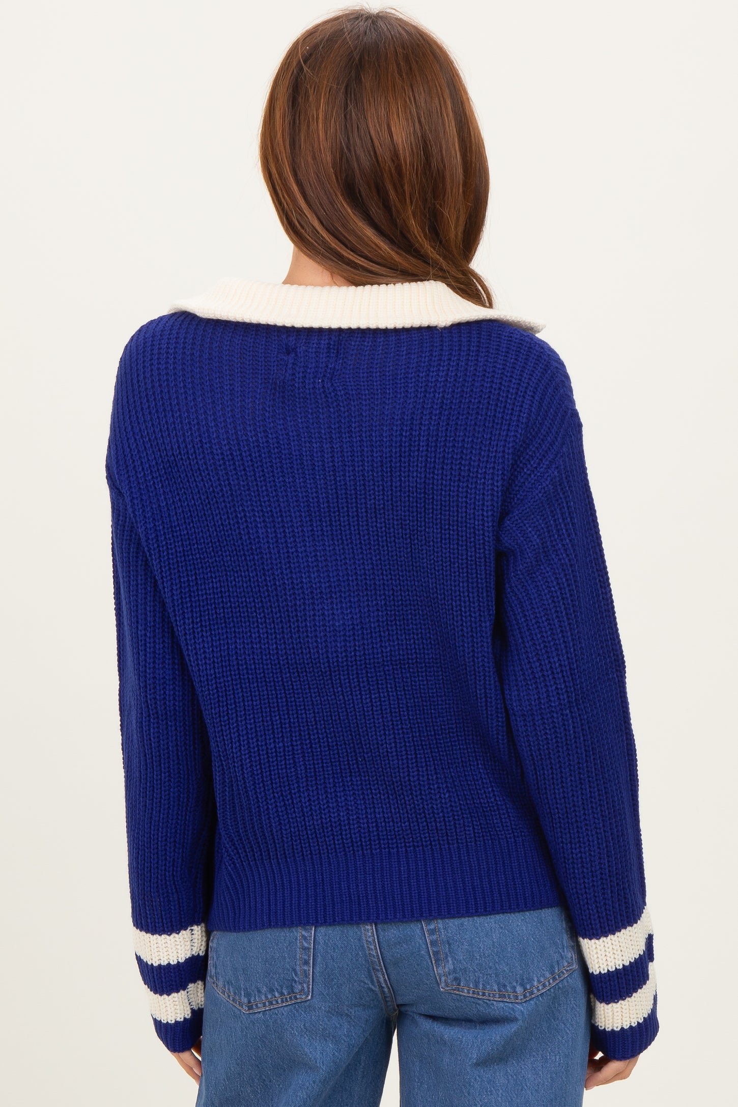 woman wearing a back view of a blue ribbed sweater with a white collar and striped cuffs