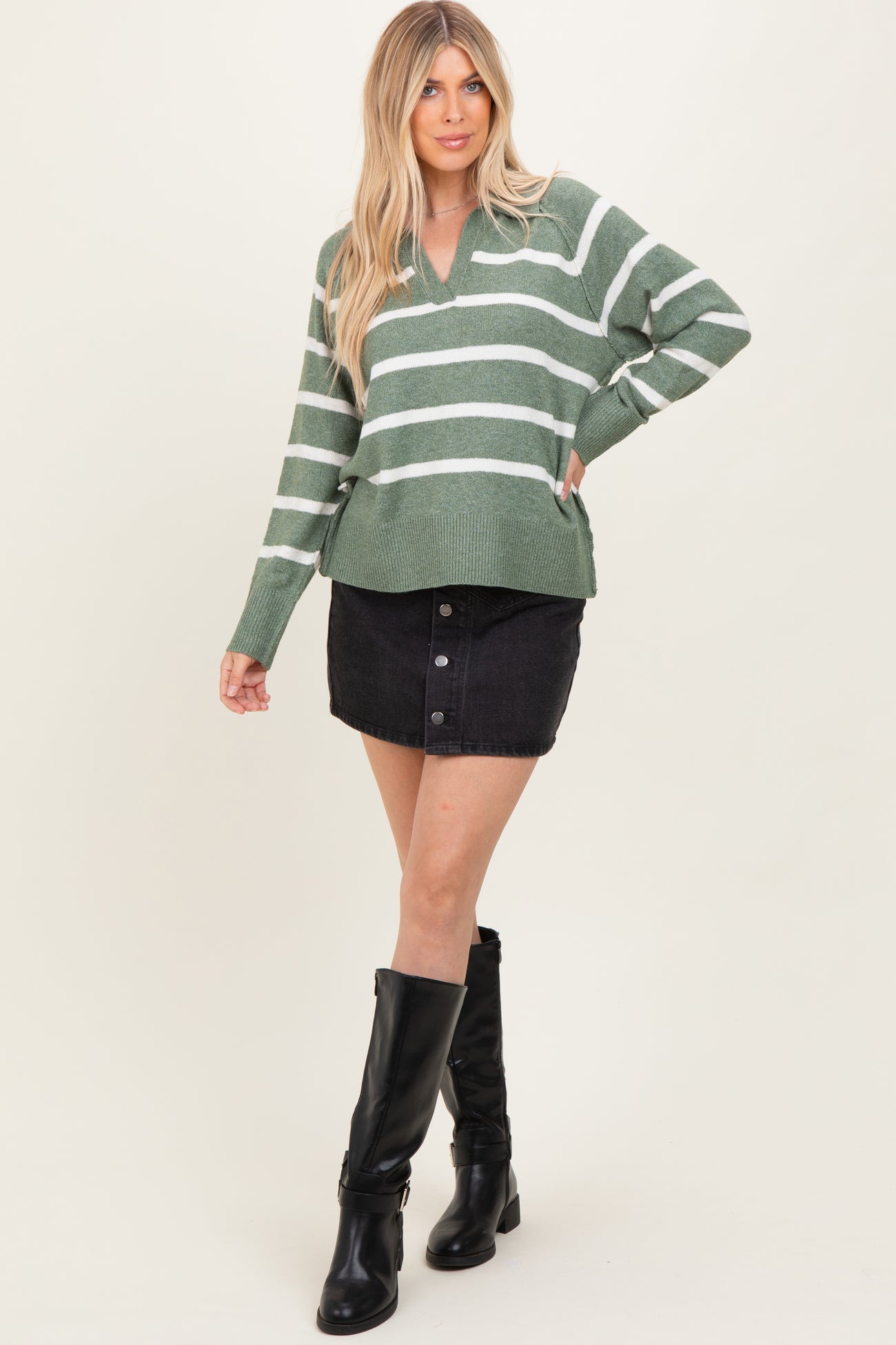 woman wearing a green and white striped oversized sweater with a v-neck and black button-up denim skirt, paired with knee-high black boots