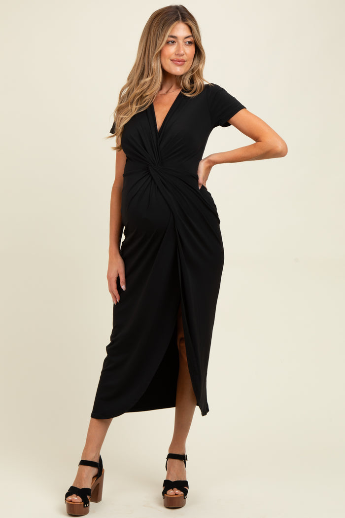 woman wearing a black short sleeve maternity dress with a twist front and side slit, showcasing her baby bump