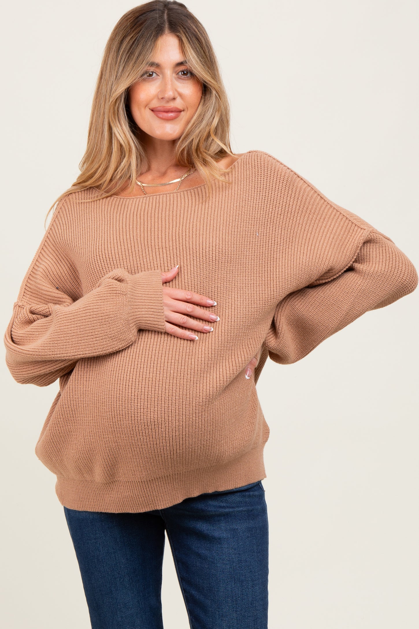 woman wearing a brown oversized ribbed maternity sweater and holding her baby bump