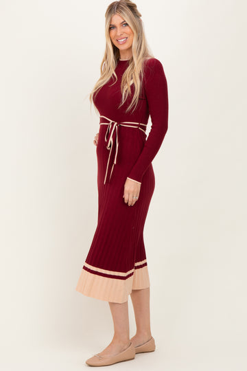 woman wearing a burgundy ribbed knit midi dress with a tie waist and beige pleated hem