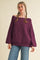woman wearing a dark purple oversized off-the-shoulder sweater with balloon sleeves and blue jeans