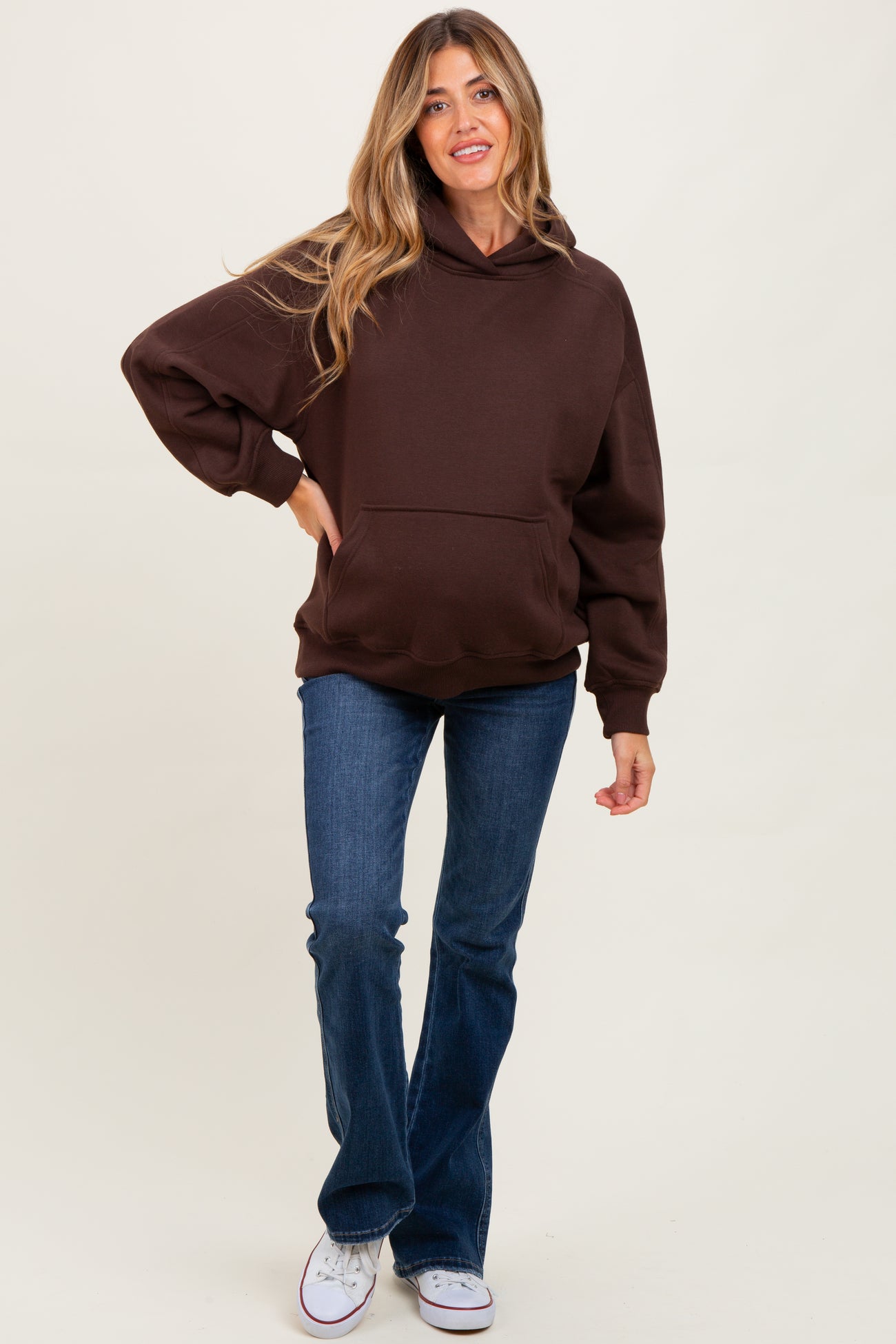 woman wearing a brown hoodie paired with blue flared jeans, styled for maternity wear