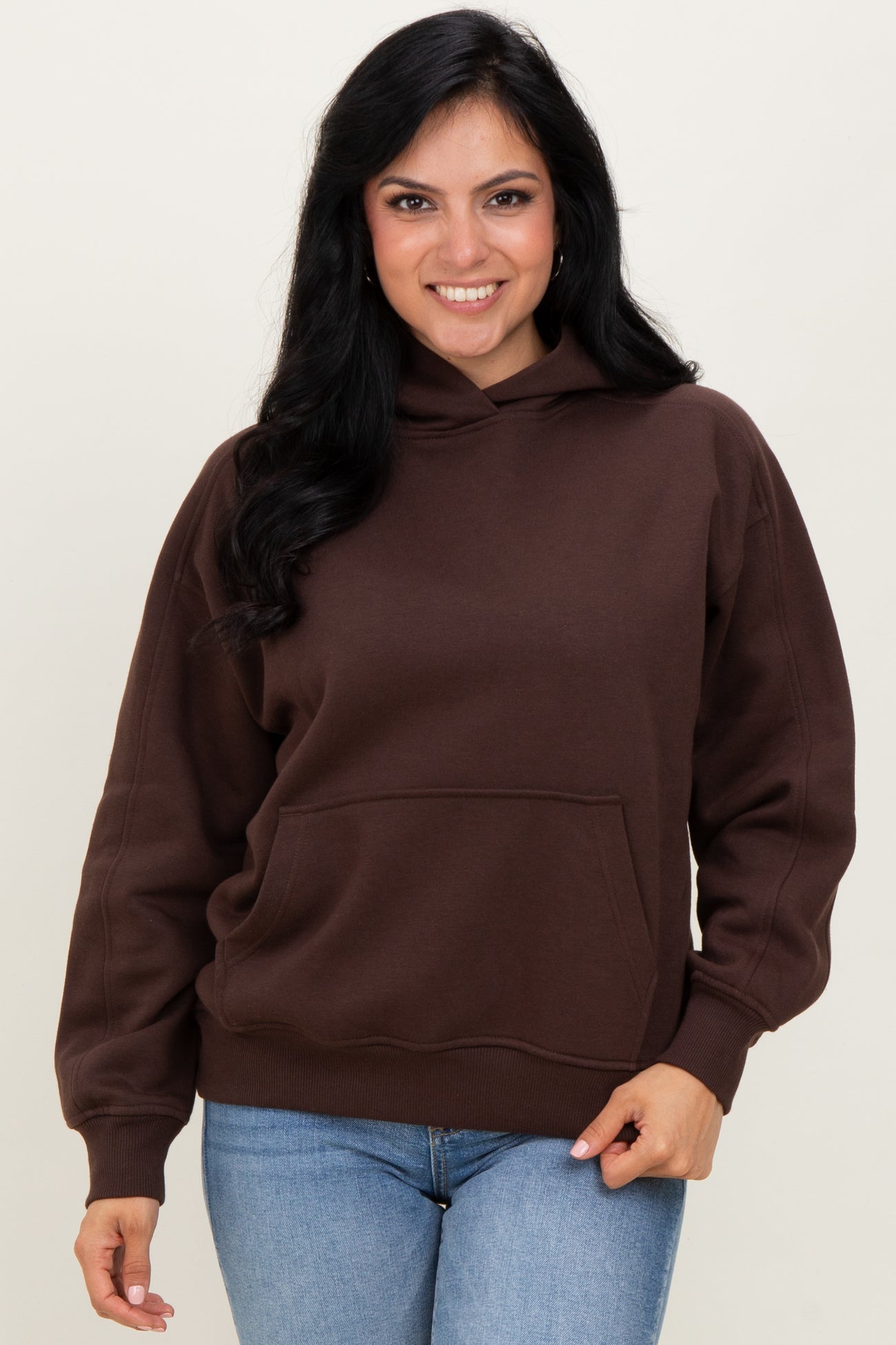 woman wearing a brown hooded sweatshirt with a front pocket and long sleeves, paired with light blue jeans