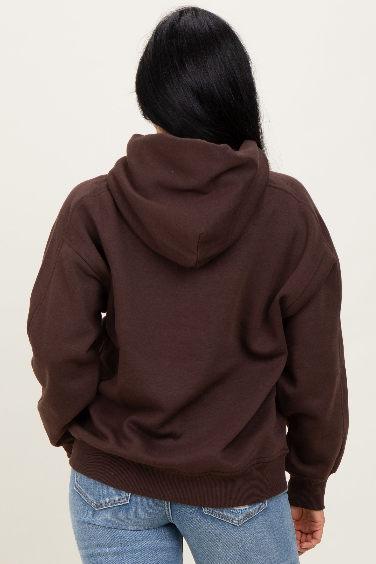 woman wearing a brown hooded sweatshirt with a relaxed fit, showing the back view
