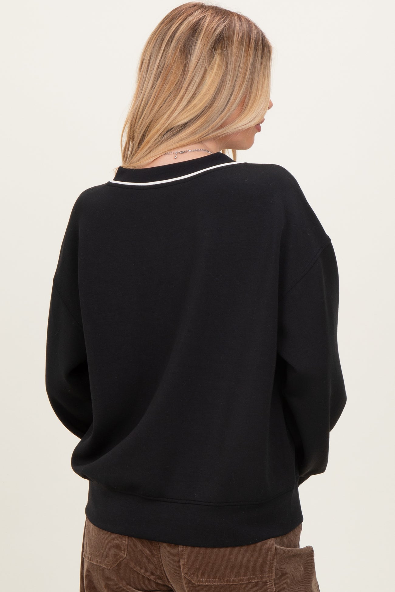 woman wearing a black oversized sweatshirt with white detail on the neckline, shown from the back