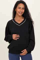 woman wearing a black maternity sweatshirt with a v-neck and white piping, holding her baby bump