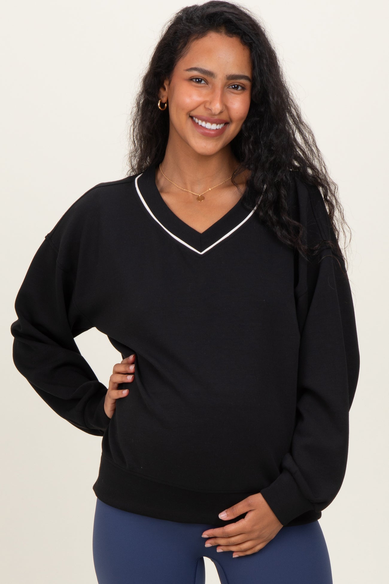 woman wearing a black maternity sweatshirt with a v-neck and white trim, holding her baby bump