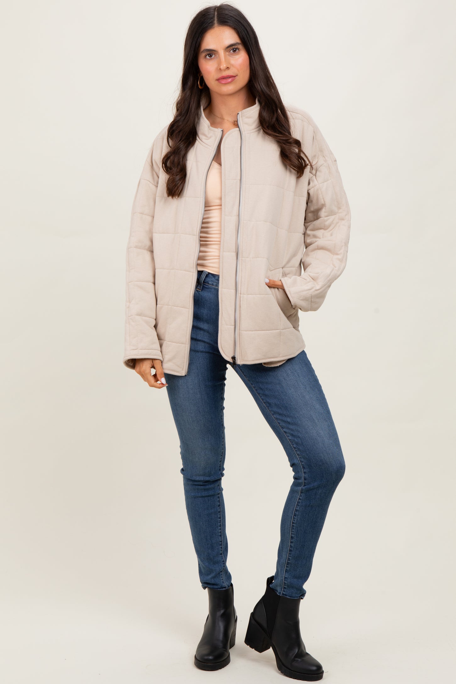 woman wearing a beige quilted jacket over a light pink top, paired with blue jeans and black ankle boots