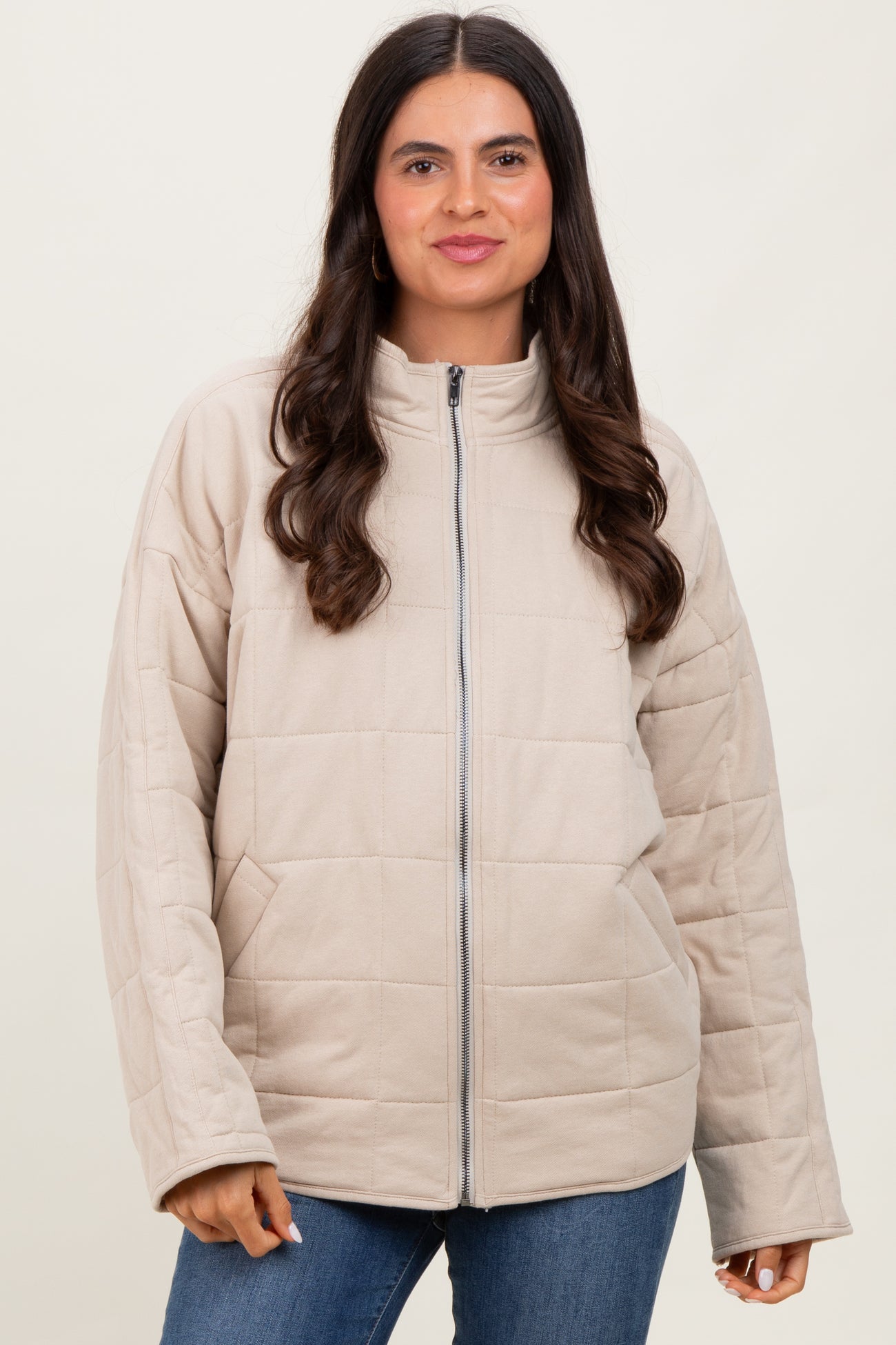 woman wearing a tan quilted zip-up jacket with a high collar and blue jeans