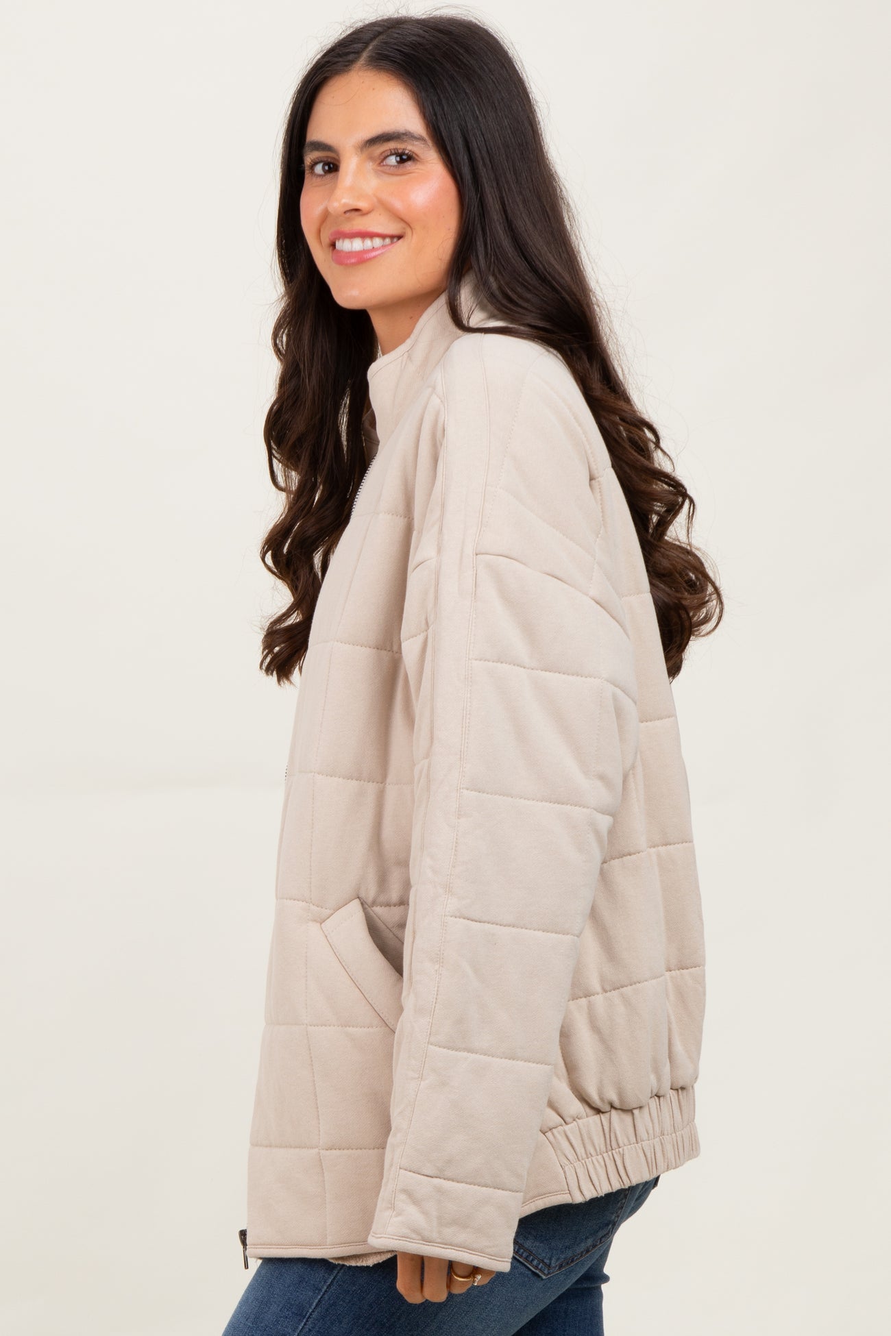 woman wearing a taupe quilted pullover jacket with a relaxed fit and side pockets, smiling against a neutral background