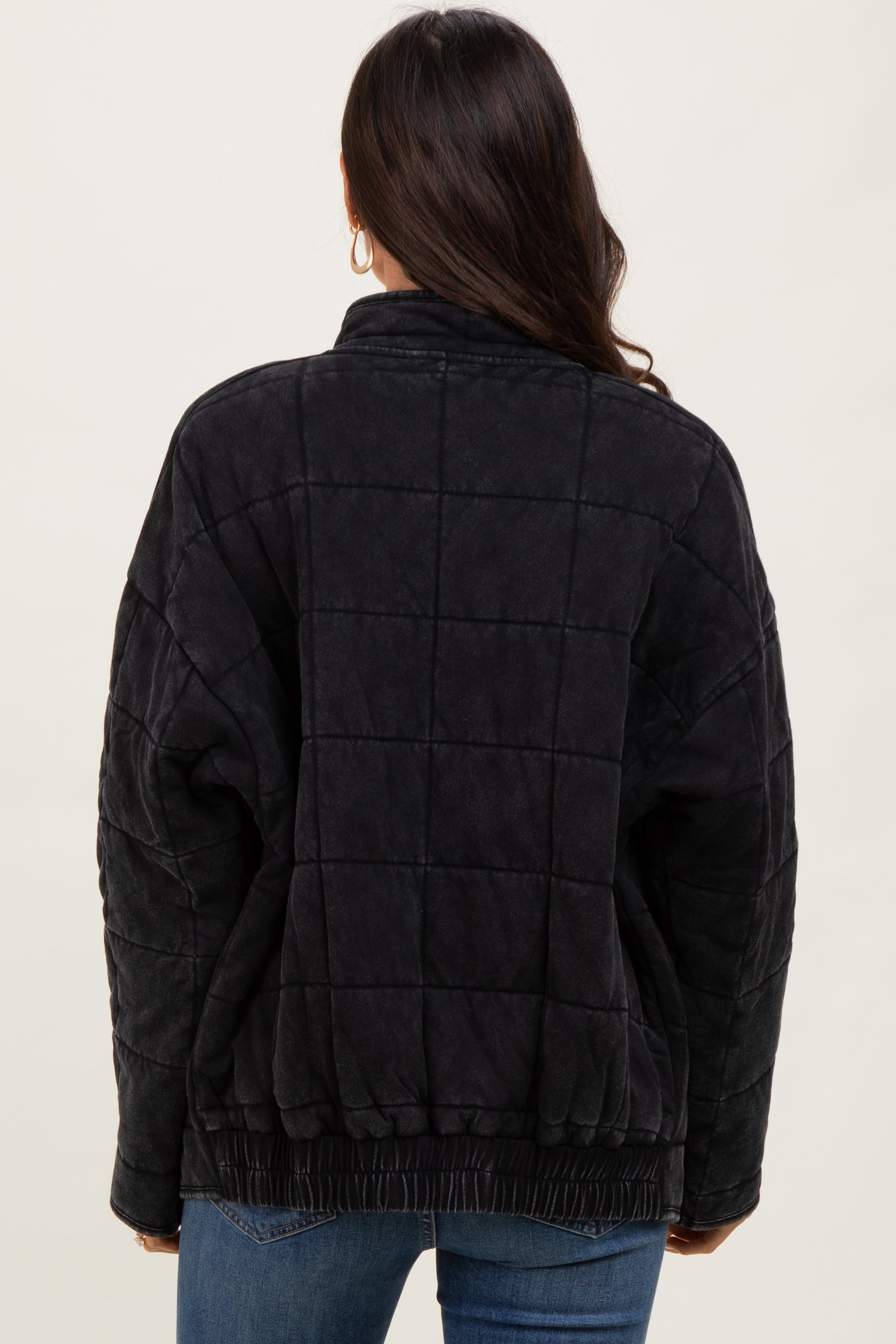 woman wearing a black quilted oversized jacket with a high collar and elastic waistband, viewed from the back