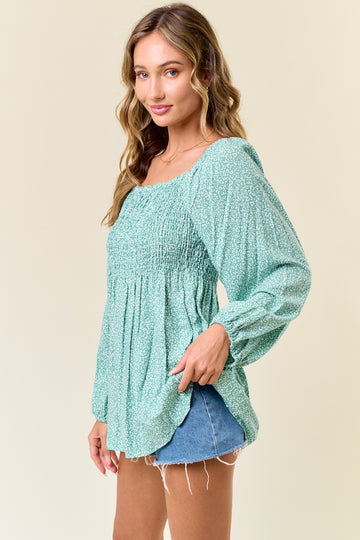 woman wearing a green floral smocked blouse with long sleeves and a relaxed fit, styled with denim shorts