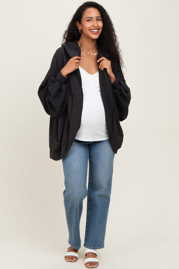 woman wearing a black oversized maternity hoodie, white v-neck top, and blue jeans, showing off her baby bump